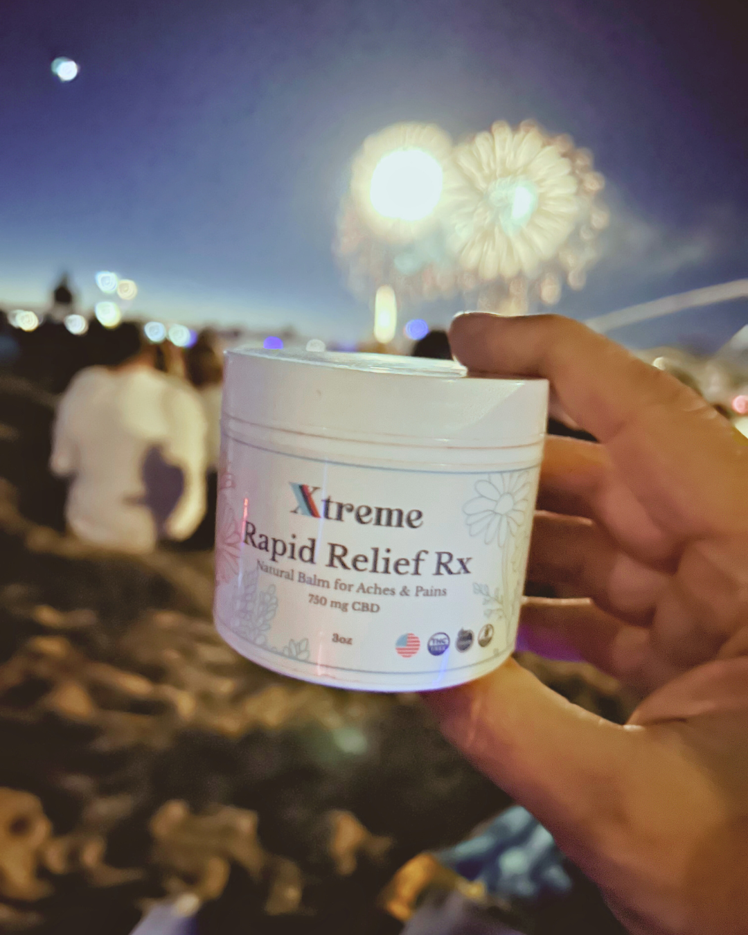 Xtreme Brands RX Rapid Relief Balm held with fireworks in the background – strongest doctor-trusted formula with full-spectrum hemp, Arnica, and Menthol for targeted pain relief.