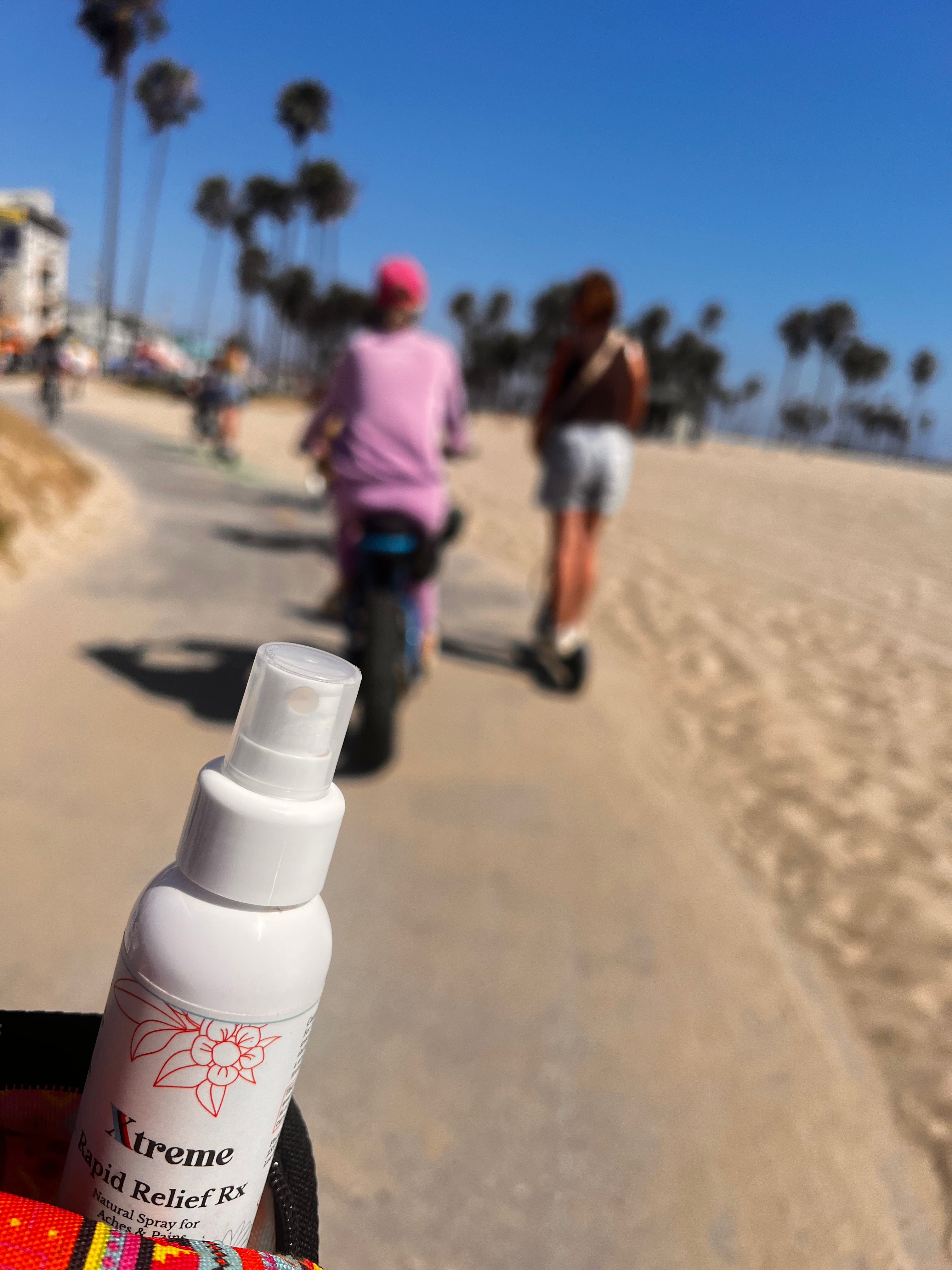 Xtreme Brands RX Rapid Relief Spray with people riding scooters and palm trees in the background – strongest doctor-trusted formula with full-spectrum hemp, Arnica, and Menthol for fast, hands-free pain relief.