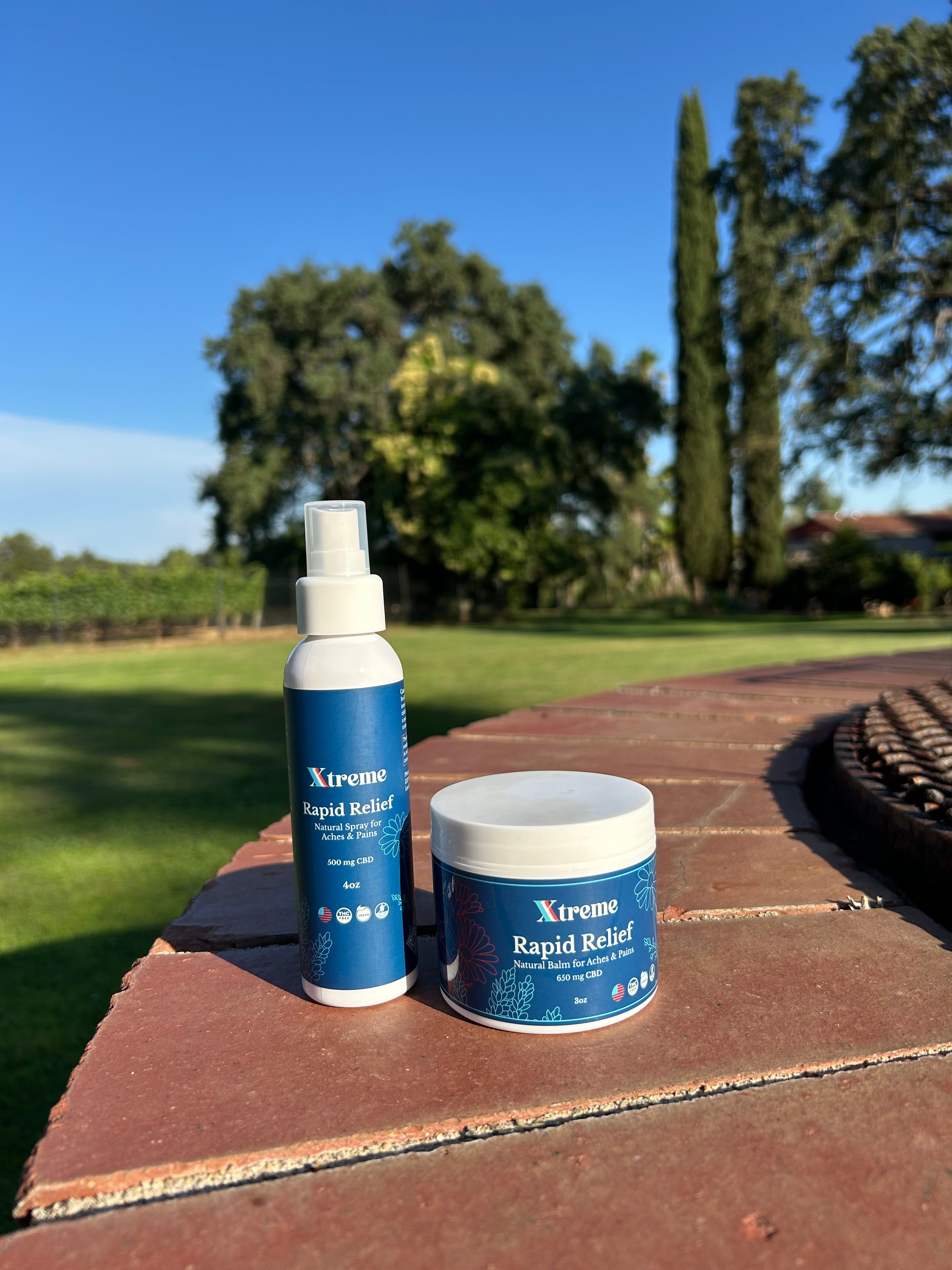 Xtreme Rapid Relief Balm and Natural Spray outdoors with trees in the background – USA-made, doctor-trusted hemp-derived CBD formulas with Arnica, Turmeric, and Willow Bark for everyday muscle and joint relief.