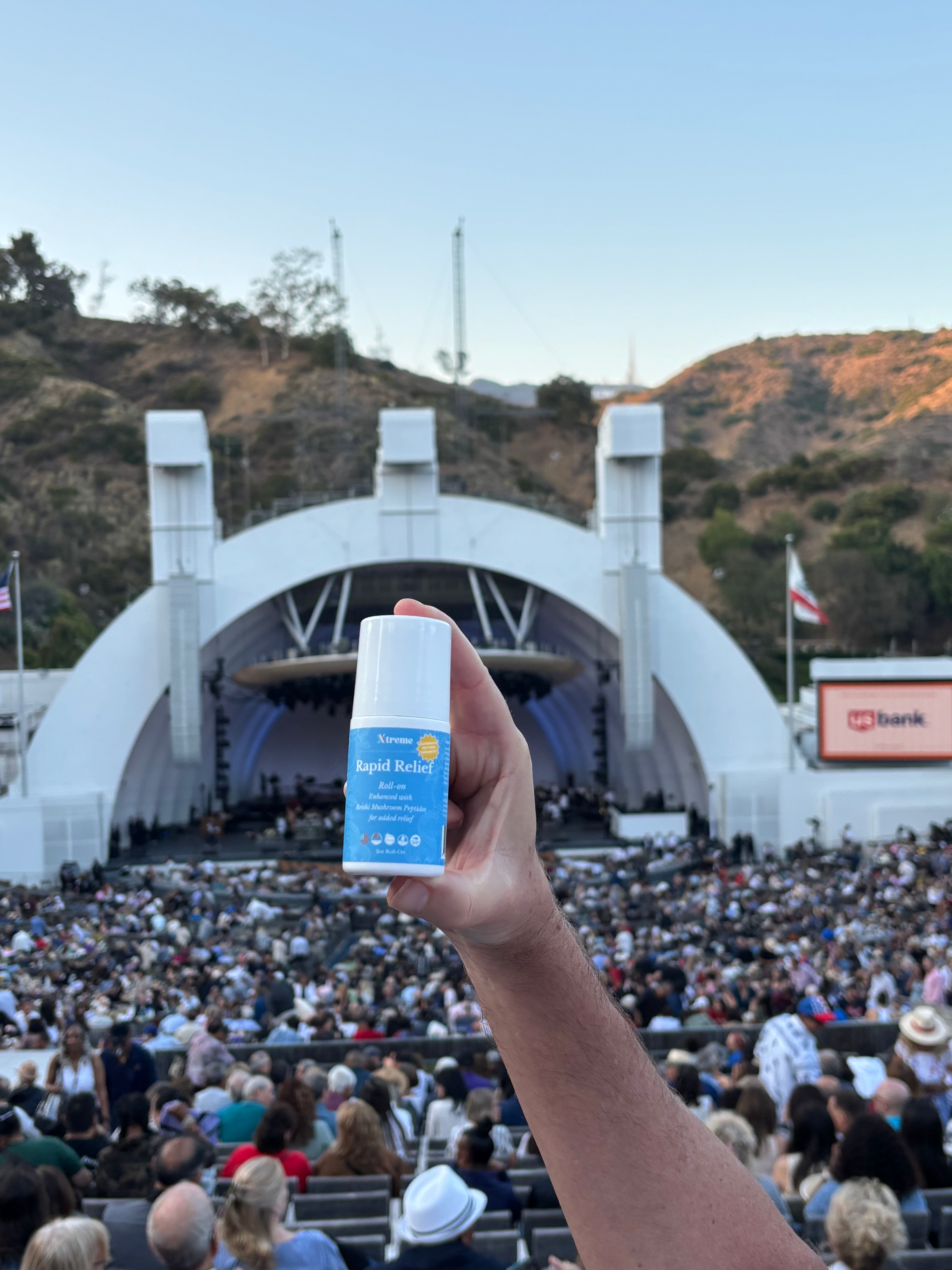 Xtreme Rapid Relief Roll-On held up at a concert – USA-made natural pain relief with full-spectrum hemp, Arnica, and Menthol for active lifestyles.
