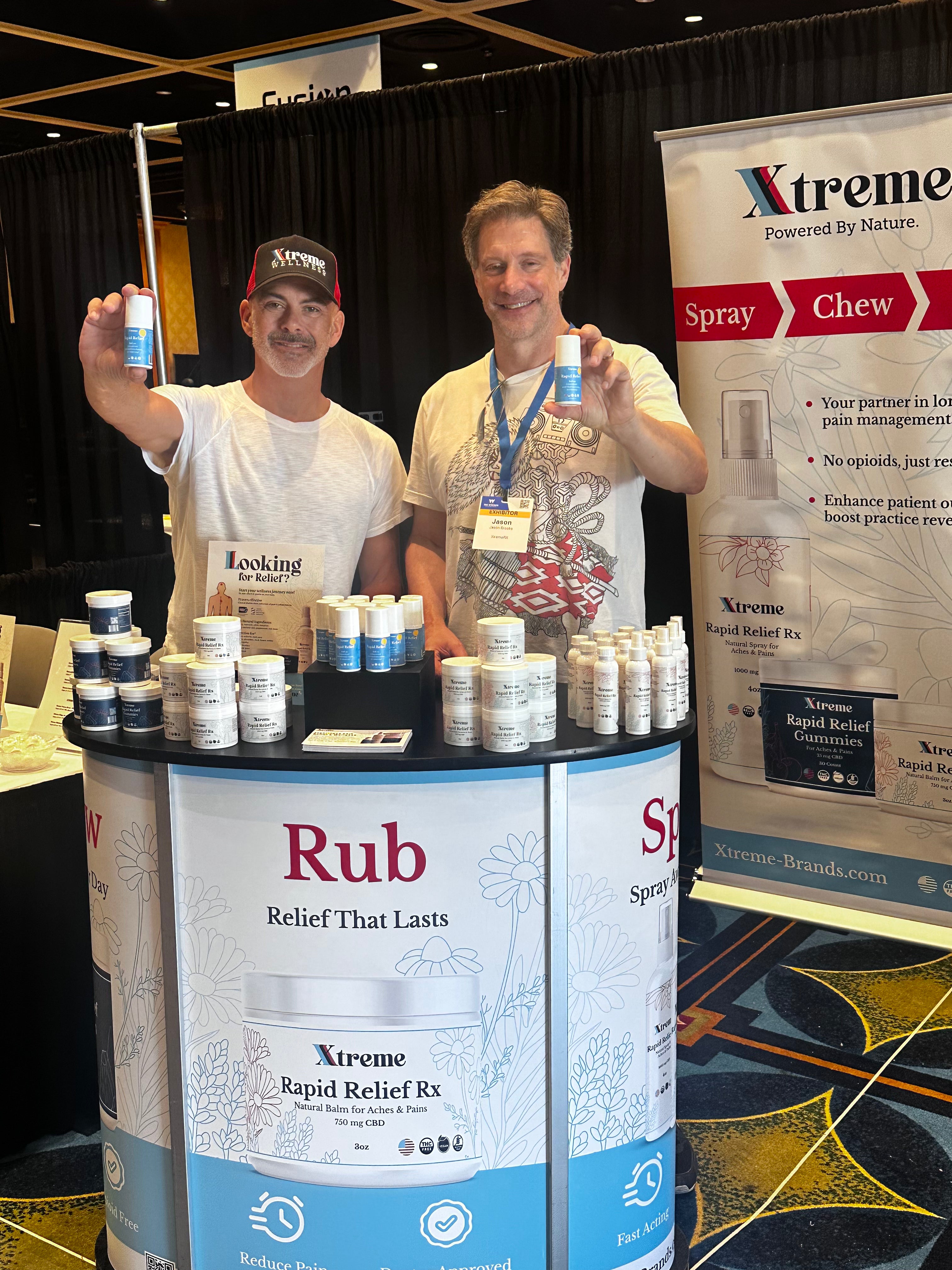 Xtreme Brands co-owners Jason Brooks, former TV star known for Baywatch Hawaii and Days of Our Lives, and Jeff Doiron holding Xtreme Brands products at a tradeshow – USA-made wellness and pain relief formulas.
